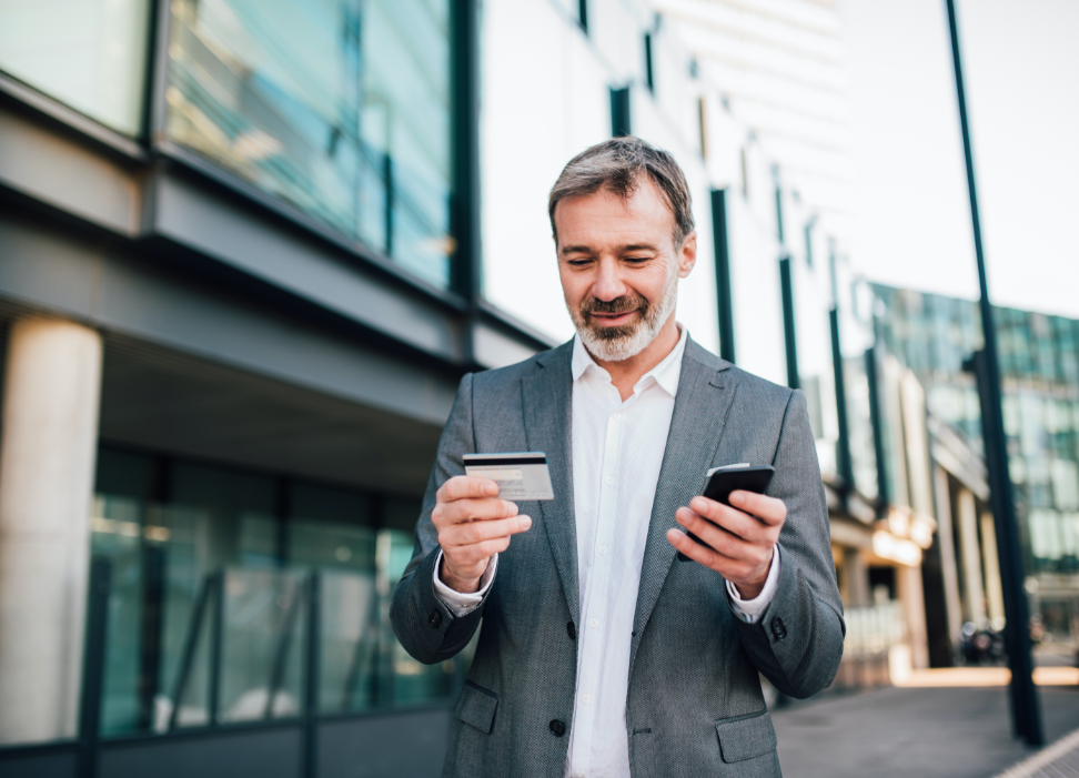 man standing outside in street looking at card while holding mobile phone
