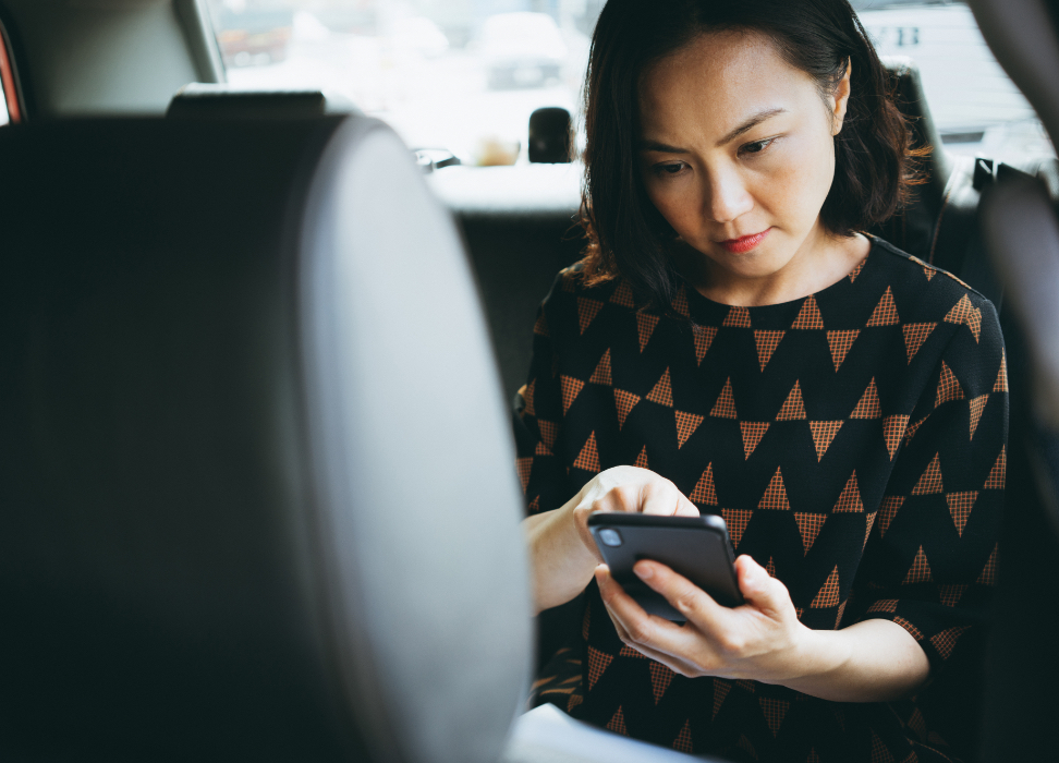 Woman sitting in the back seat of a car looking at mobile device.