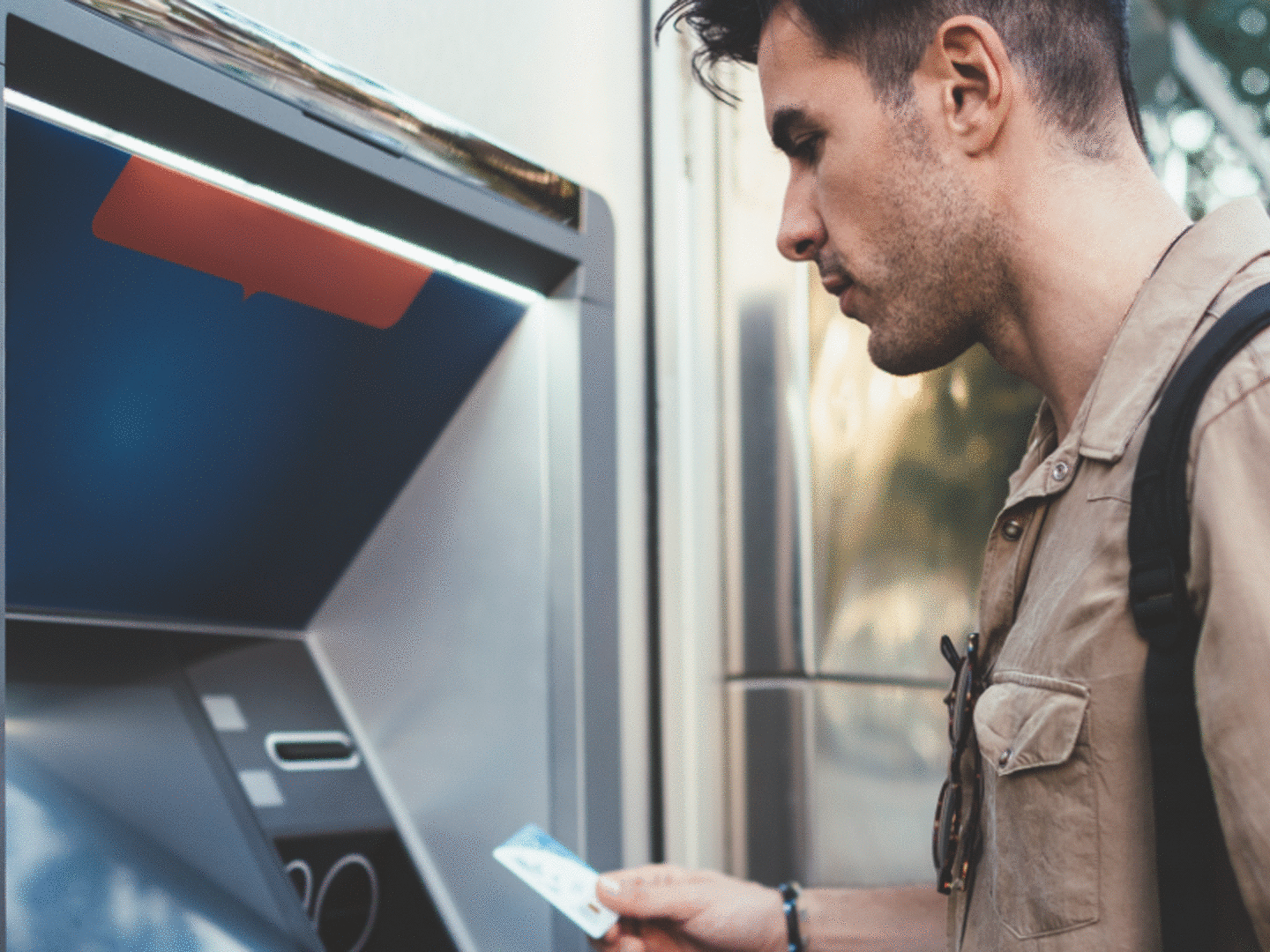 Man standing in front of ATM machine with card in hand looking at screen.