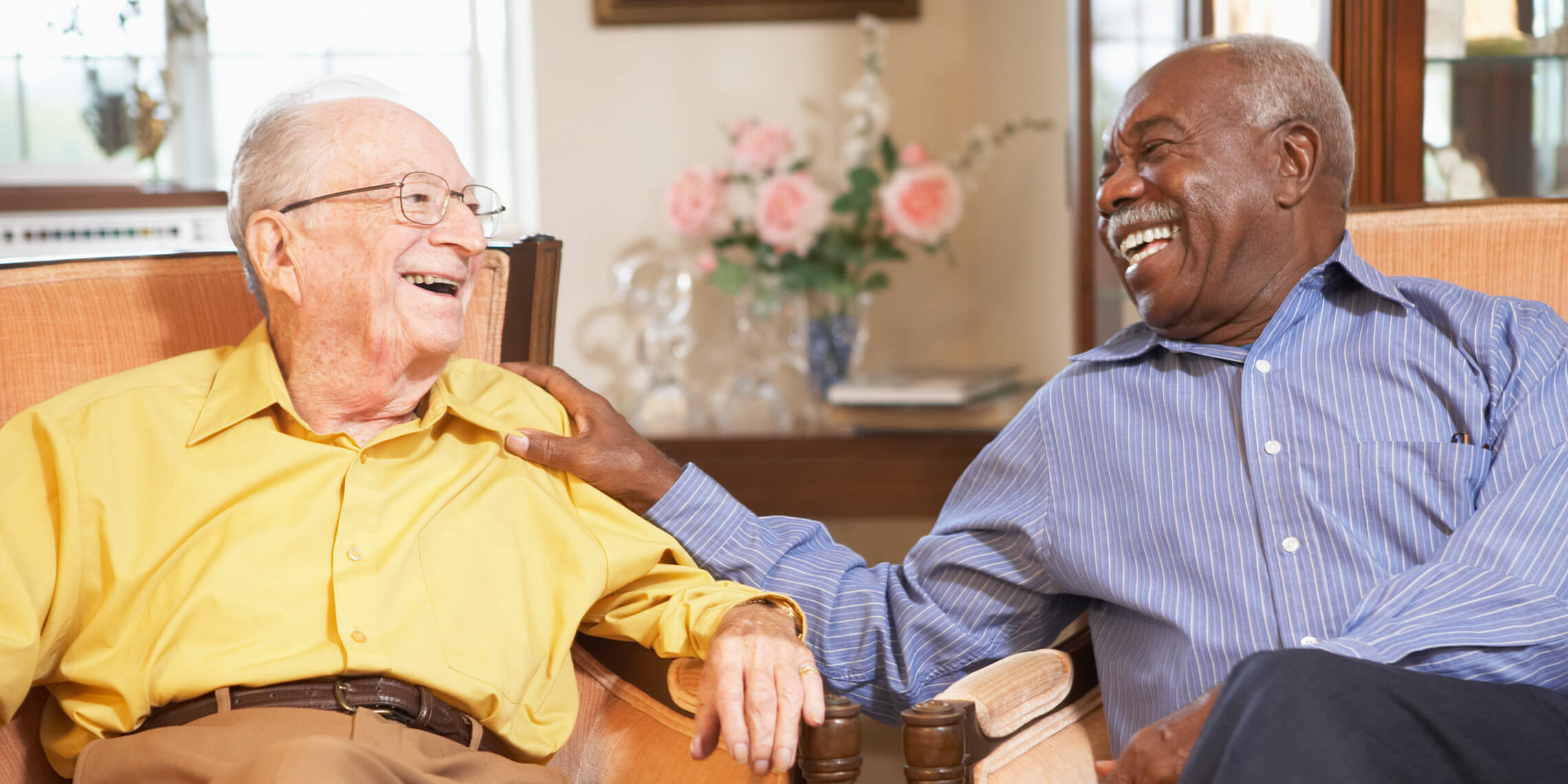 old gay couple sitting in living room laughing