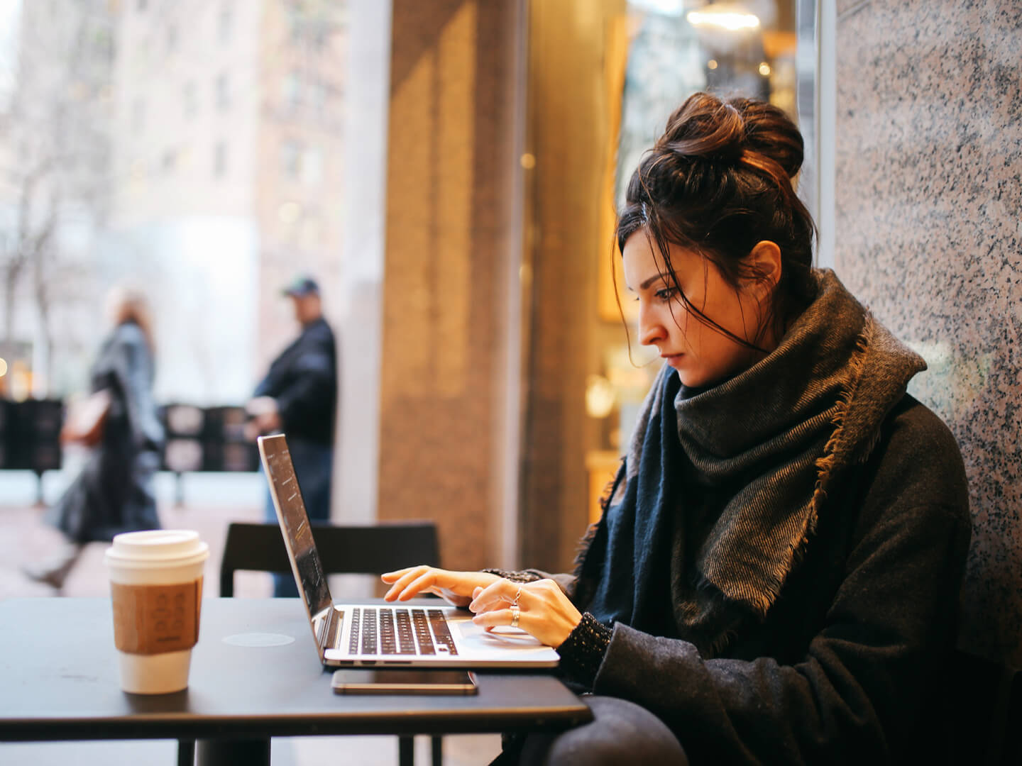young woman using laptop outside a cafe to access online banking for webster connect checking account